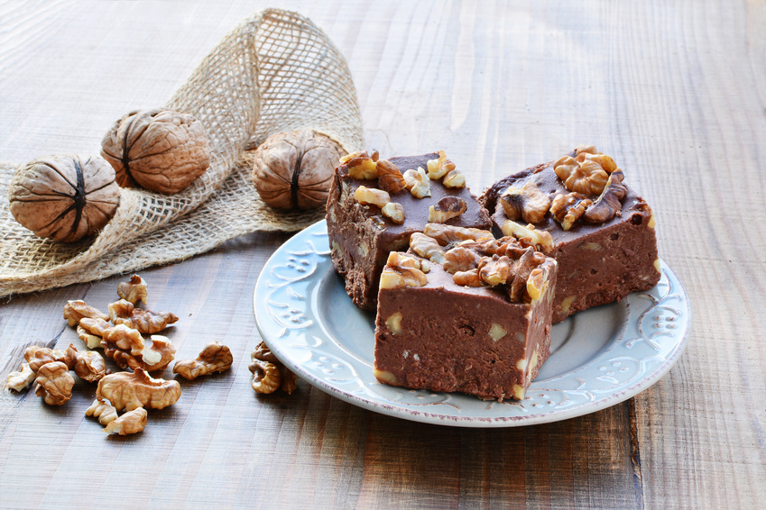 Homemade chocolate fudge with walnuts on plate over wooden table.